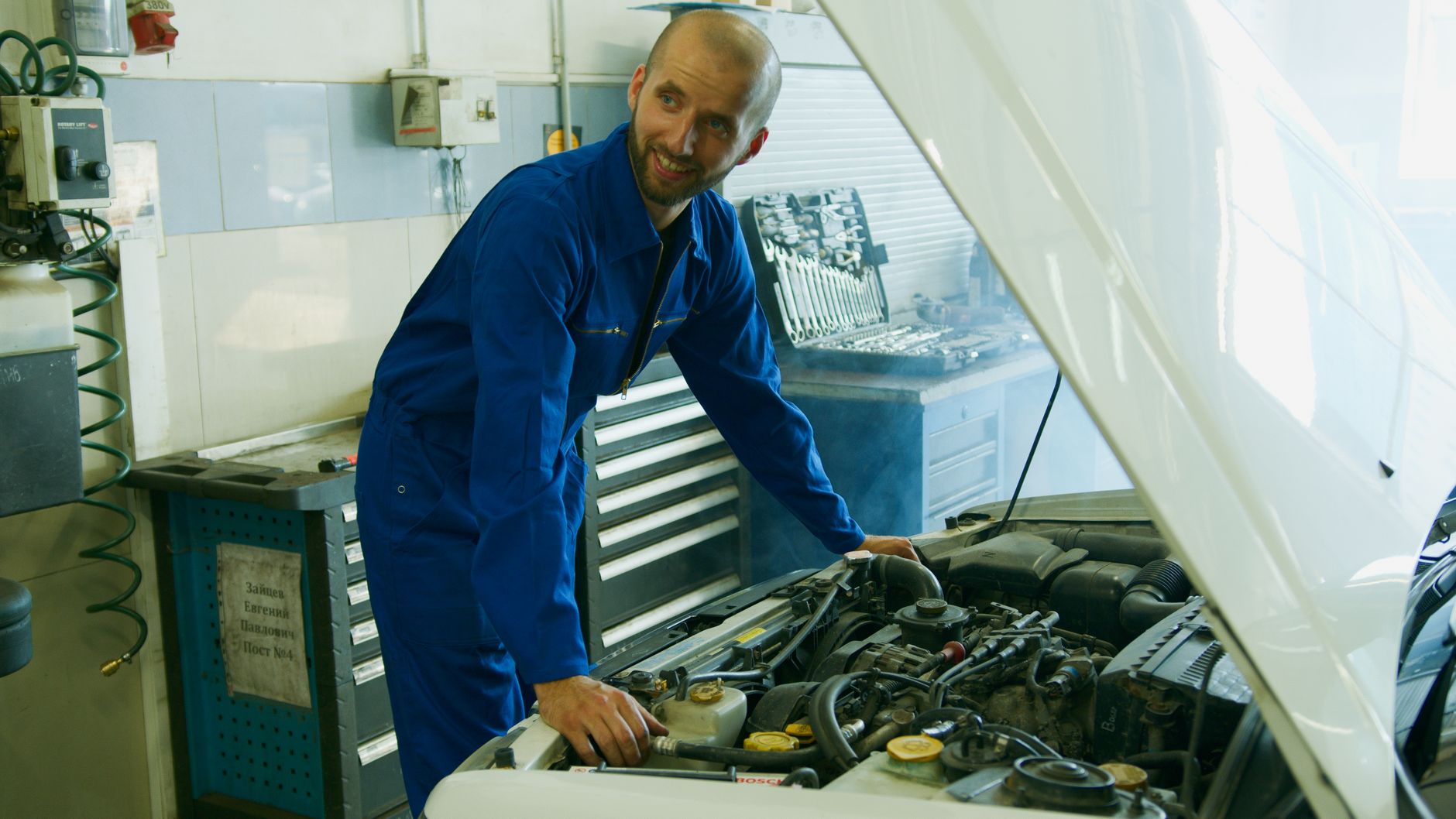 A mechanic working under the hood of a car in an auto shop